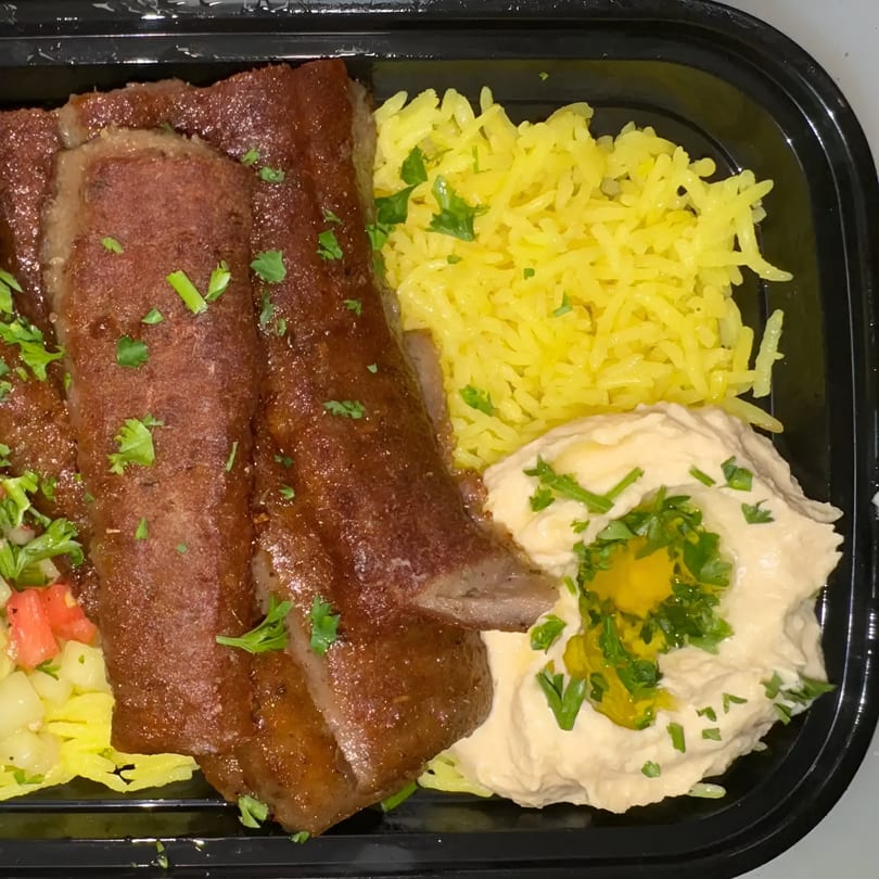 Taza Grill's Mediterranean dish with sliced meat, yellow rice, hummus, and a side salad.