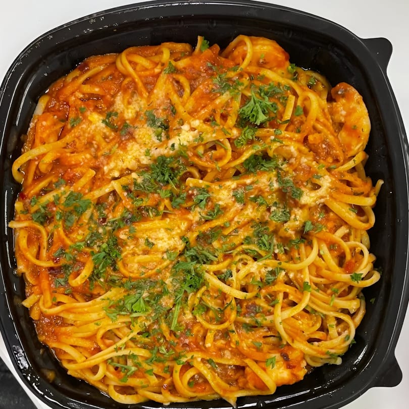 Taza Grill's Mediterranean pasta with red sauce, cheese, and fresh parsley in a black container.