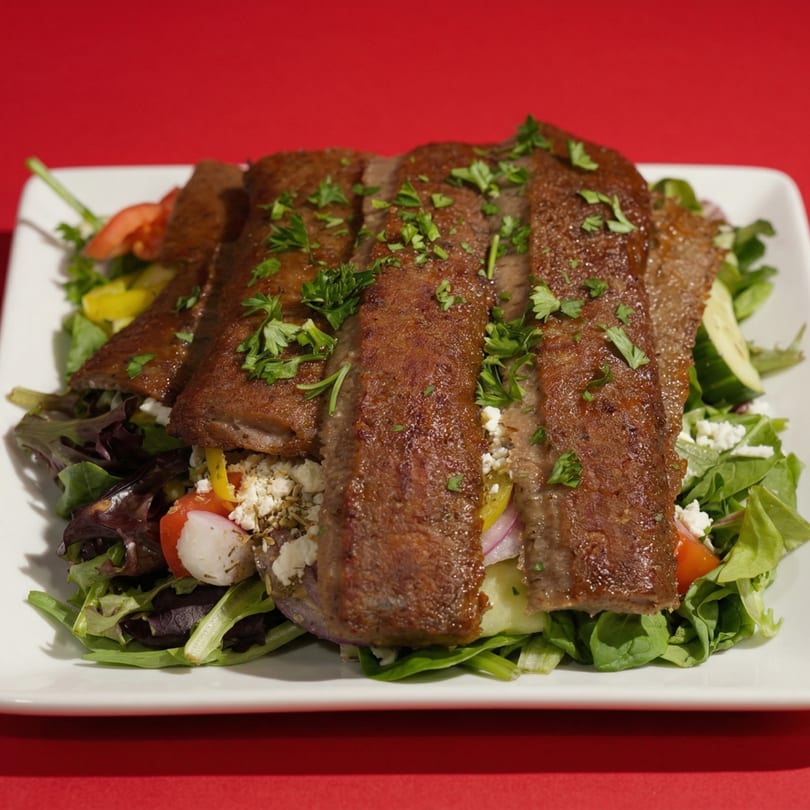 A white rectangular plate holds a gyro salad with meat slices, lettuce, tomatoes, and feta cheese.